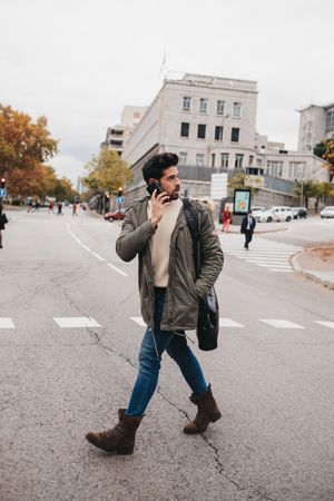 Busy male with smartphone crossing road