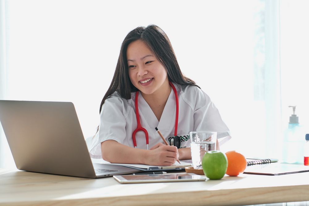 Cheerful Asian doctor browsing laptop in medical office
