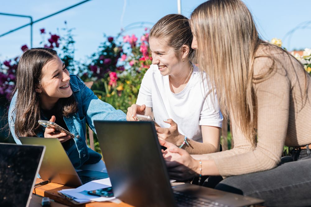 College woman taking a break from studying showing messages on phones while talking and laughing.