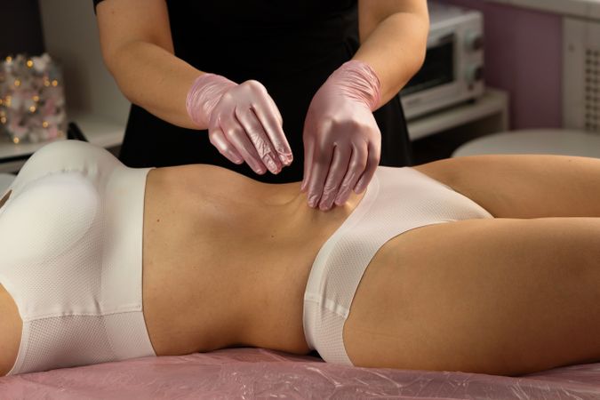 Aesthetician performs abdominal massage wearing pink protective gloves.