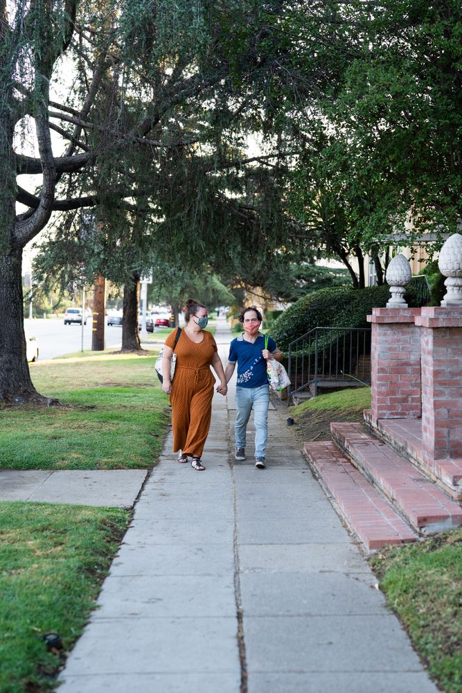 Loving couple walking together holding hands and wearing masks on sidewalk