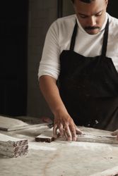 Man in apron working with slices of brownies on marble counter