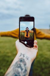 Crop hand taking photo of woman in field