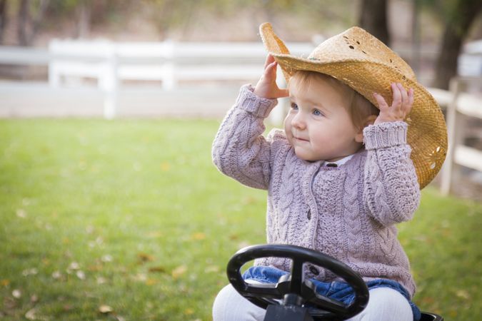 Toddler Wearing Cowboy Hat and Playing on Toy Tractor Outside