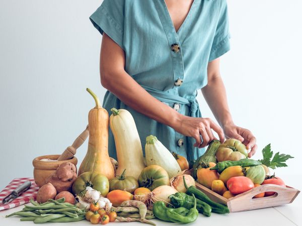 Crop woman putting raw vegetables on kitchen table