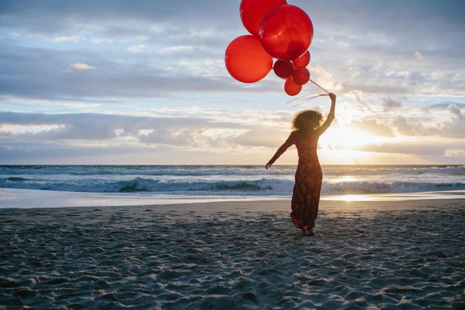 Rear view of a woman walking along on the beach holding balloons