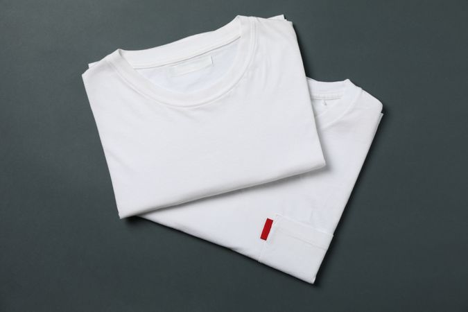 Folded white t-shirts on light dark background, space for text