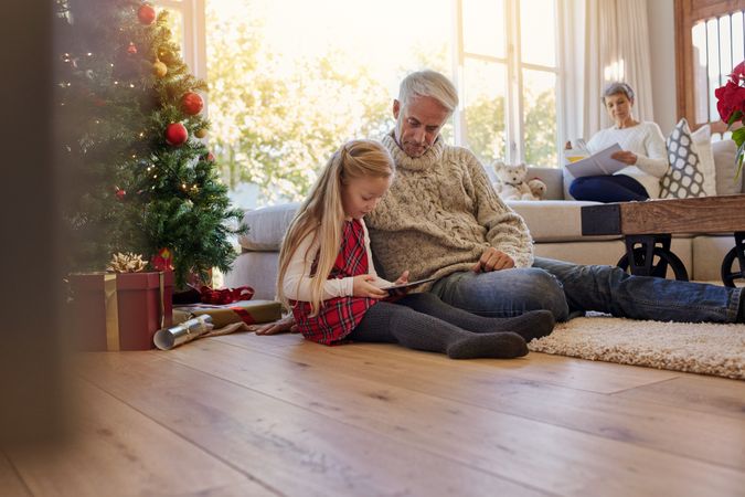 Little girl with grandfather using digital tablet at home during Christmas
