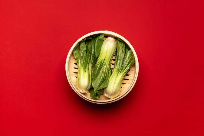 Bok choy cooked in bamboo steamer, above view on a red table