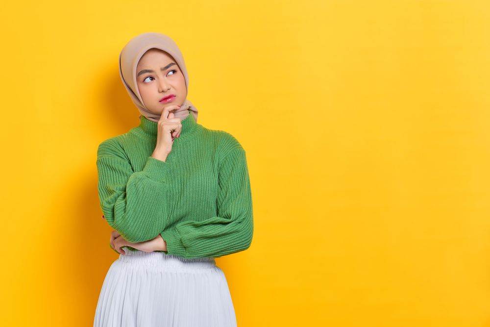 Woman in headscarf deep in thought with hand on her cheek with copy space