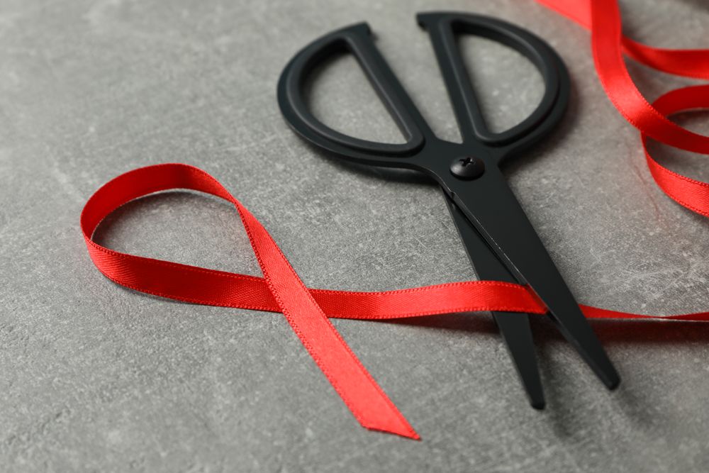 Awareness red ribbon and scissors on grey background, copy space