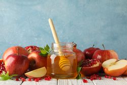 Apple halves, pot of honey with dipper and pomegranates on table