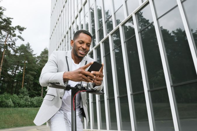 Smiling Black man riding scooter and speaking on smartphone