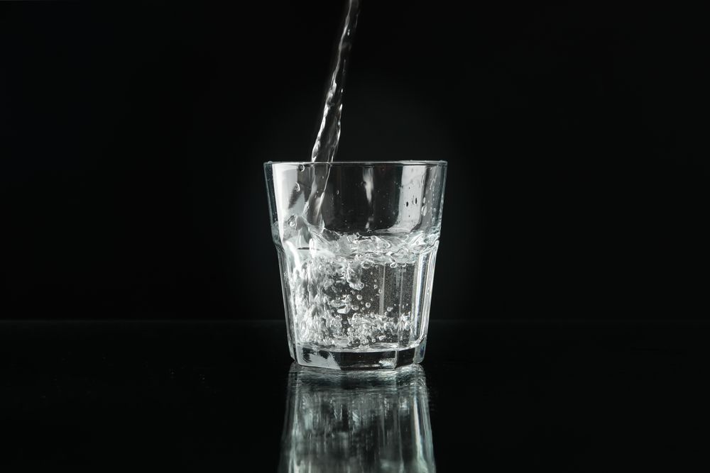 Glass of water being poured in dark room, copy space