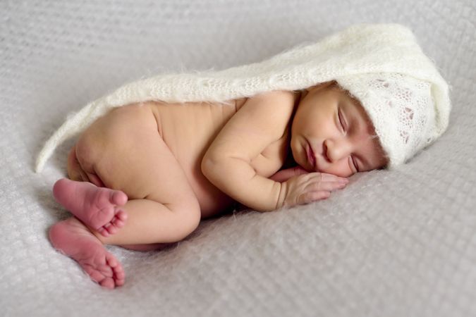 Close-up of a newborn baby girl, sleeping on a gray blanket and a white bonnet