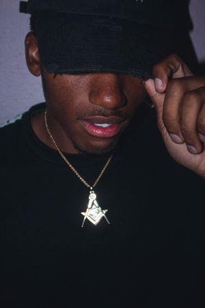Black man in dark cap and shirt wearing the illuminati symbol necklace