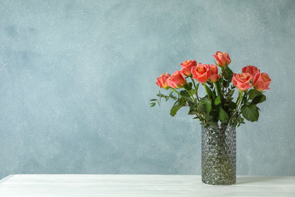 Vase with orange roses on table against light background, space for text