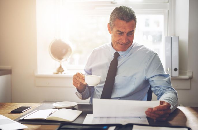 Man in business attire sipping coffee while looking over documents