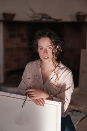 Portrait of young female artist with hands on canvas