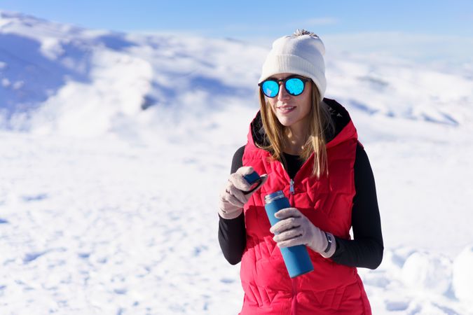 Woman in snowsuit opening water bottle on snowy mountain