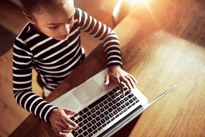 Top view of girl concentrating while working on laptop in sunny kitchen