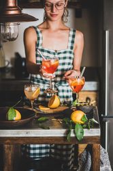 Young woman in checkered dress and glasses holding aperitif with orange slices