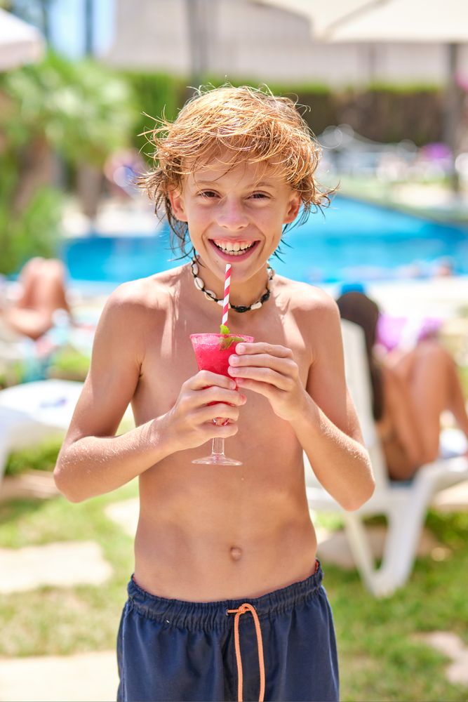 Shirtless boy smiling and holding drink at resort