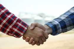 Businessmen shake hands against silos. Agriculture business