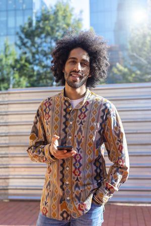 Black man holding a mobile phone while standing outdoors on a sunny day