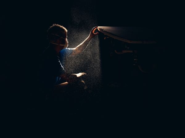 Man checking smoothness of surfboard in dark workshop