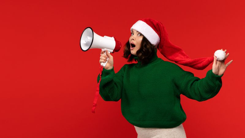 Excited woman in Santa hat holding megaphone and shouting.