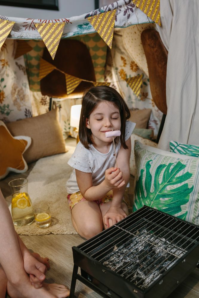 Little girl camping at home and smelling a roasted marshmallow
