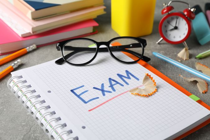 Open notebook with the word “exam” with glasses resting on notebook