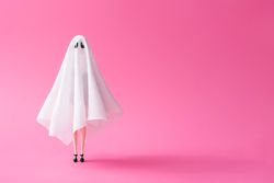 Doll under ghost sheet costume against pastel pink background