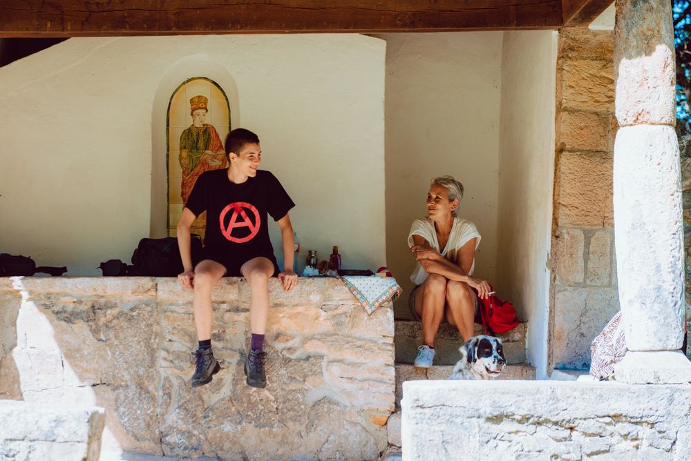 Young woman sitting on stone fence and speaking with older woman on steps of houses