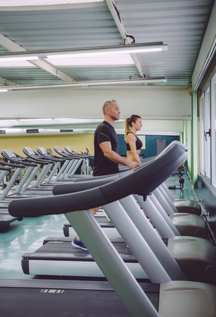 Side view of male and female working out on treadmills in quiet gym