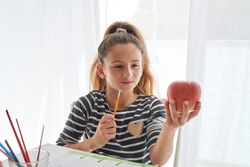 Girl with paintbrush looking at apple