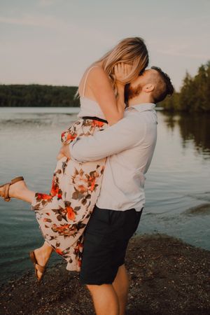 Loving man carrying happy woman on hands on shore