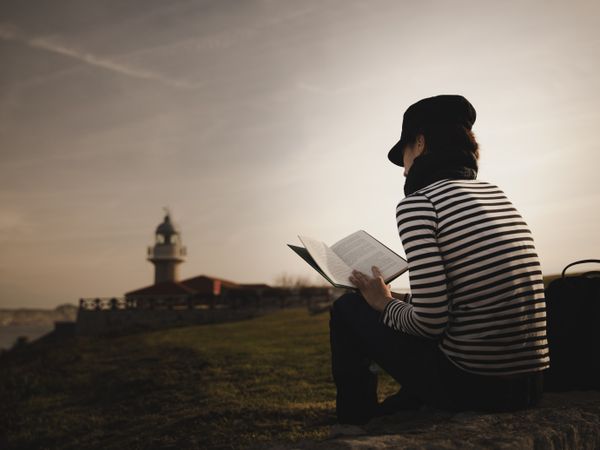 Woman with book on grass near lighthouse