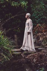 Woman in mesh dress stepping onto rocks on pond