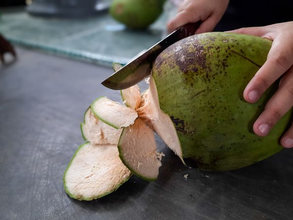 Hand Peeling Young Coconut with Large Knife to Access Coconut Water