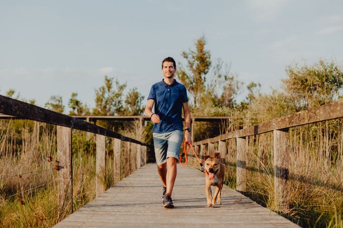 Happy adult man walking with dog along countryside