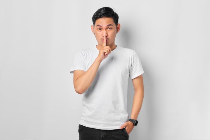 Asian male in grey studio making “shhh” sign