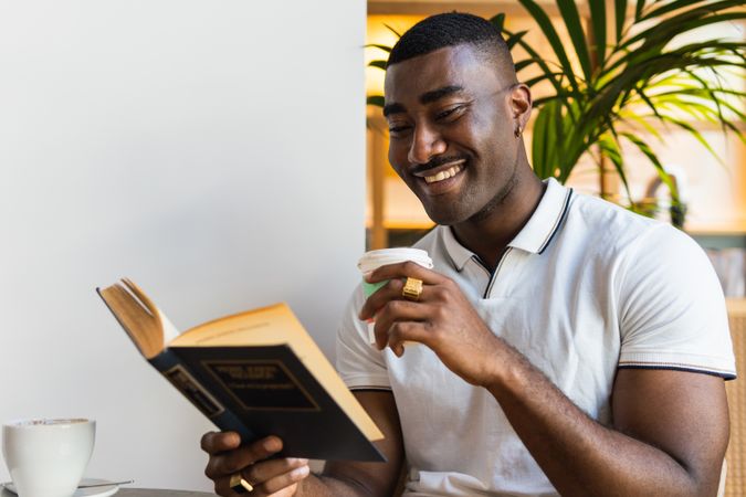 Smiling Black man reading book with drink in cafe