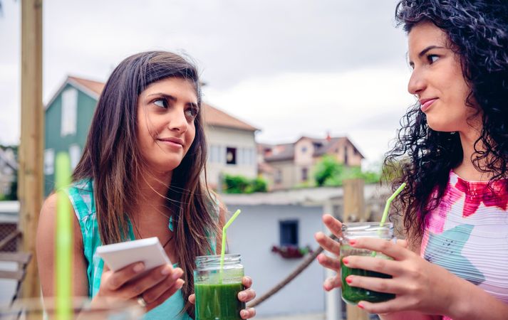 Two incredulous female friends sipping cocktails outside