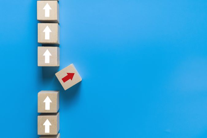 wooden blocks with up arrows and one different direction red arrow isolated on blue background. leadership concept