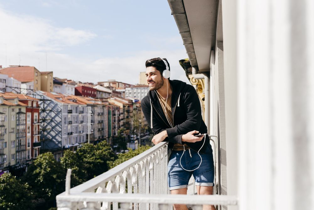 Young happy man holding smartphone on balcony
