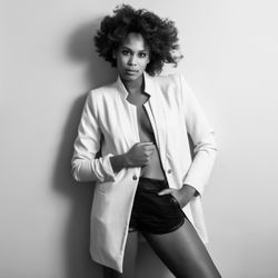 Monochrome shot of female with curly hair in pajamas standing against light wall
