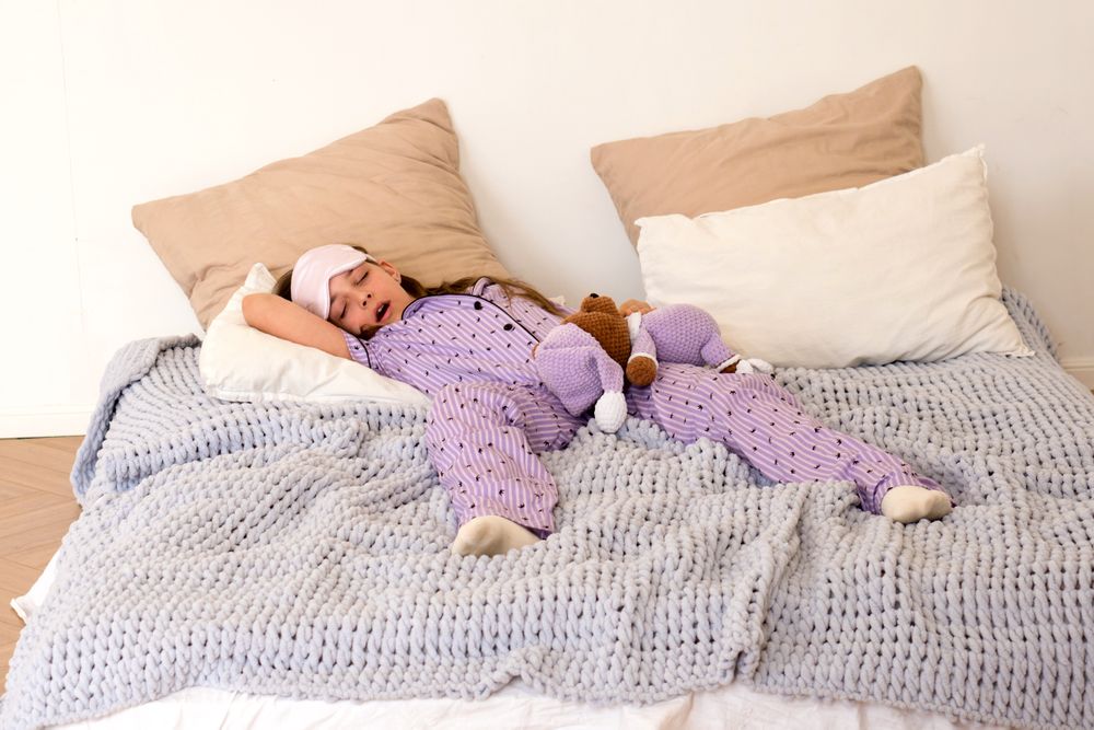 Girl napping in bed with teddy bear in purple pajamas.