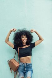 Female wearing casual clothes leaning on turquoise wall and smiling while raising her hands